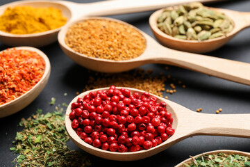 Different aromatic spices in spoons on black table, closeup