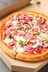 Tasty pizza with smoked sausages and mushrooms in cardboard box on table, closeup