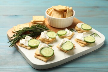Tasty crackers with cream cheese, rosemary and cucumber on light blue wooden table, closeup