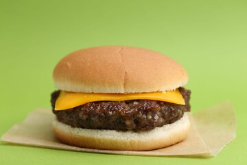 Cheeseburger with tasty patty on green background, closeup