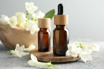 Bottles of essential oil and jasmine flowers on grey table, closeup