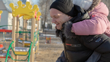 Grandfather playing with her granddaughter on the playground in the park in winter