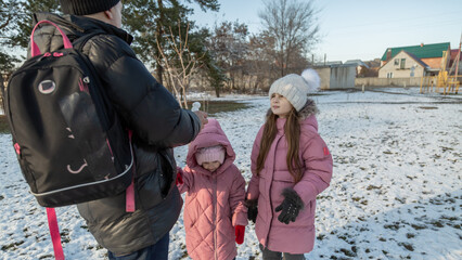 Grandfather walks with his granddaughters after school in the park in sunny winter day