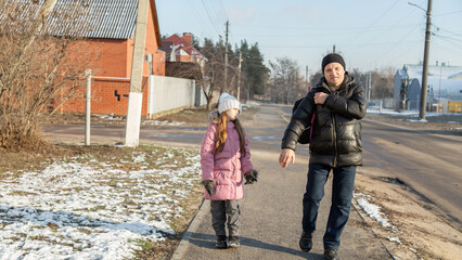 Grandfather walks with his granddaughters after school in the park in sunny winter day