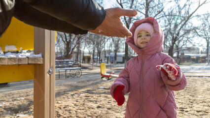 Grandfather playing with his granddaughter on the playground in the park in winter