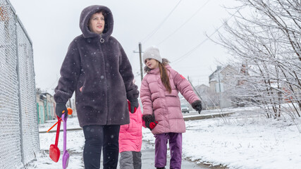 Grandmother and girls walk along a snowy street in winter
