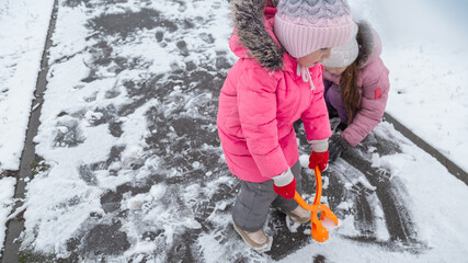 Two little girls in colorful clothes play outdoors during a snowfall.