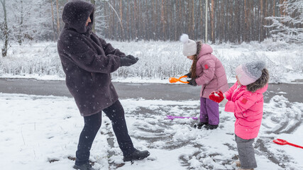Grandmother with grandchildren in warm clothes playing outdoors in winter park, enjoying snowy...