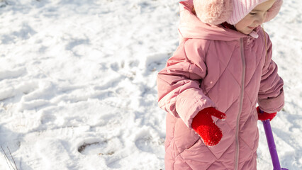 Cheerful positive child girl wearing a outerwear smiling walking through a snowy countryside forest