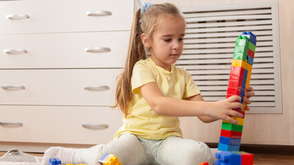 Little girl playing with colorful toy blocks in room at home.