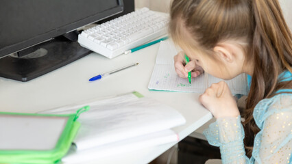 Little school girl sit at table at home write in exercise book prepare homework alone.