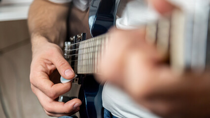 Fototapeta premium Guitar music. The performer plays. Practice chords. Male performer hands with fingers studying melody of song on electric string guitar fretboard indoors.