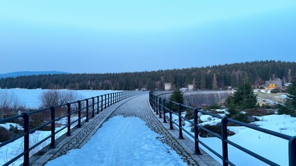 A Beautiful Scenic Winter Bridge Gracefully Spanning Over a Frozen Lake at Dusk Time
