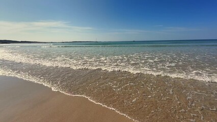 Tranquil Beach Scene Featuring Gentle Waves, a Clear Blue Sky, and Warm Sunlight Above