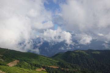 Amidst towering mountains, clouds drift lazily across the sky while sunlight illuminates the...