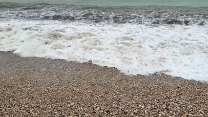 Experience serene beach waves lapping against a pebbly shoreline, perfect for relaxation