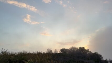 Fototapeta premium The tranquil sunset over the rolling hills is adorned with soft clouds drifting gently