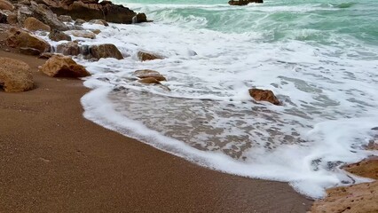 Experience the serene beach waves gently flowing over the rugged rocky shoreline beautifully