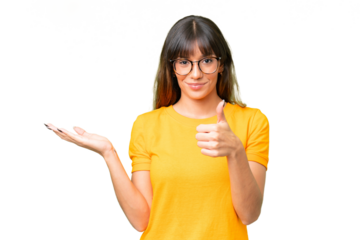 Young caucasian woman over isolated chroma key background holding copyspace imaginary on the palm to insert an ad and with thumbs up