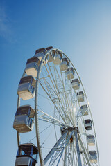 A large Ferris wheel rises into the air with cabins against a blue sky. A Ferris wheel with enclosed cabins.