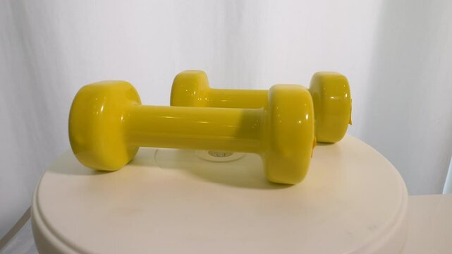  Vinyl dumbbell yellow 1 kg weight, on a rotary table, sports dumbbell spins. On a white background.