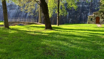 A picturesque and serene park landscape featuring a charming stone pavilion with lush, green grass