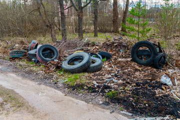 Car tires in the garbage dump on the grass near the forest. Garbage, waste in the nature. Concept polluting nature and city park.