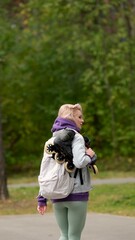 Fototapeta premium Beautiful blonde woman walking through city park holding roller skates enjoying beautiful day
