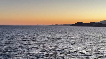 A stunning seaside sunset lights up calm waters next to an impressive city skyline
