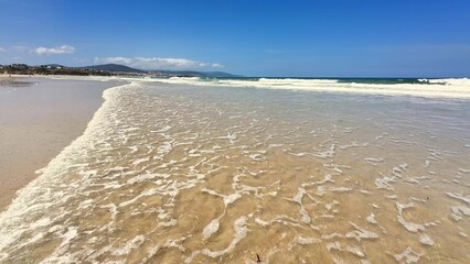 A Beautiful Sandy Shore with Gentle Waves Tumbling Under a clear and Bright Blue Sky