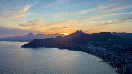 Witness a stunning aerial sunset over majestic coastal mountains and the tranquil waters