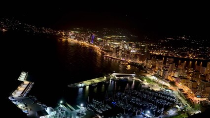 Experience the stunning night view of a coastal cityscape illuminated by vibrant lights
