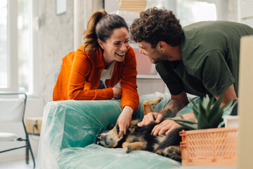 Happy couple petting dog on sofa in new home during moving day