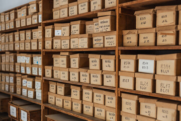 Numerous labeled cardboard boxes are neatly arranged on wooden shelves, suggesting a systematic filing system within an archive or storage facility. - obrazy, fototapety, plakaty