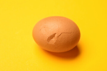 One egg with cracked shell on yellow background, closeup
