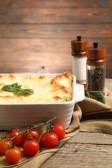 Delicious spinach lasagna in baking dish and ingredients on wooden table