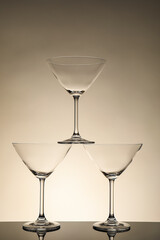 Three empty clean glasses on mirror surface against beige background