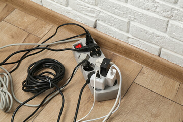 Extension power board overloaded with plugs on wooden floor, closeup