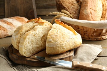 Different loaves of fresh bread, knife and spikes on wooden table, closeup
