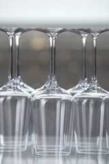 Upturned empty clean glasses on mirror surface against blurred background, closeup. Bokeh effect