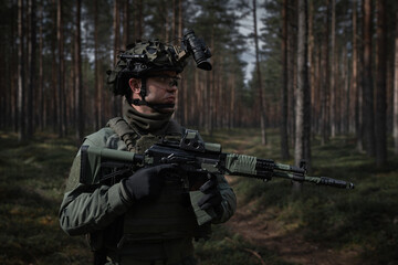 Fototapeta premium Fully equipped soldier in camouflage gear and helmet with night vision goggles holds an assault rifle during patrol in a dense forest.