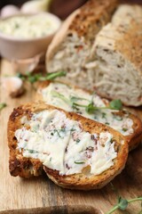 Tasty bread with garlic, herbs and oil on wooden board, closeup