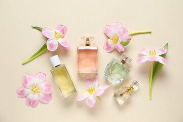 Bottles of perfume and beautiful flowers on beige background, flat lay