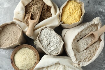 Different types of flour in bags on grey textured table, flat lay
