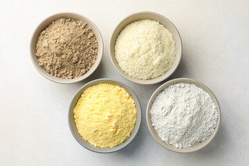 Different types of flour in bowls on light grey table, flat lay