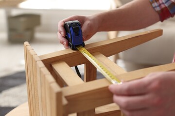 Man measuring wooden stool with tape indoors, closeup