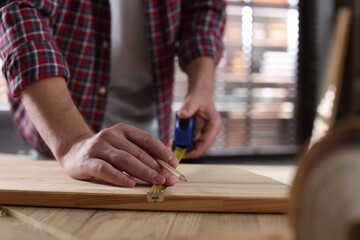 Man measuring wooden plank with tape indoors, closeup