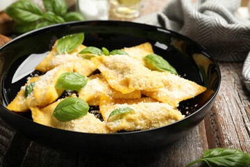 Delicious ravioli with parmesan cheese and basil on wooden table, closeup