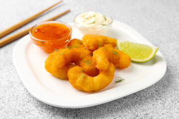 Tasty tempura shrimps, lime and sauces on grey textured table, closeup