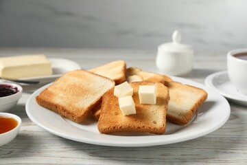 Slices of tasty toasted bread with butter on light wooden table against grey background, closeup